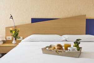 Ein ordentlich gemachtes Bett mit weißen Leinen, einem Holzkopfende und einem Tablett mit Croissants, Orangensaft und einer Tasse auf dem Nachttisch.