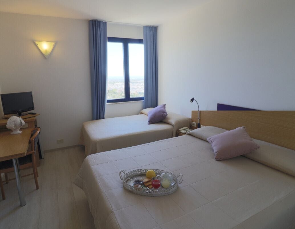 A hotel room with two beds, a desk with a computer, and a tray of breakfast items.