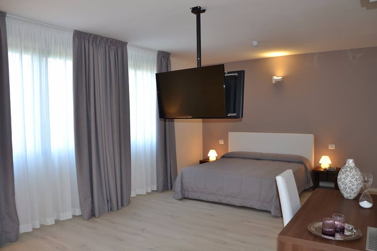 A hotel room with a bed, bedside lamps, a flat-screen TV mounted on the wall, a wooden table with a tray, and a vase.