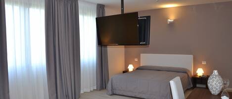 Habitación de hotel con cama, lámparas de noche, televisor de pantalla plana montado en la pared, mesita de madera con bandeja y un florero.