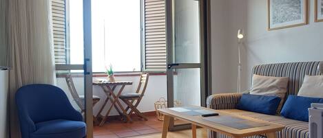 A modern living room with a blue armchair, a striped sofa, a wooden coffee table, and a large window with blinds.