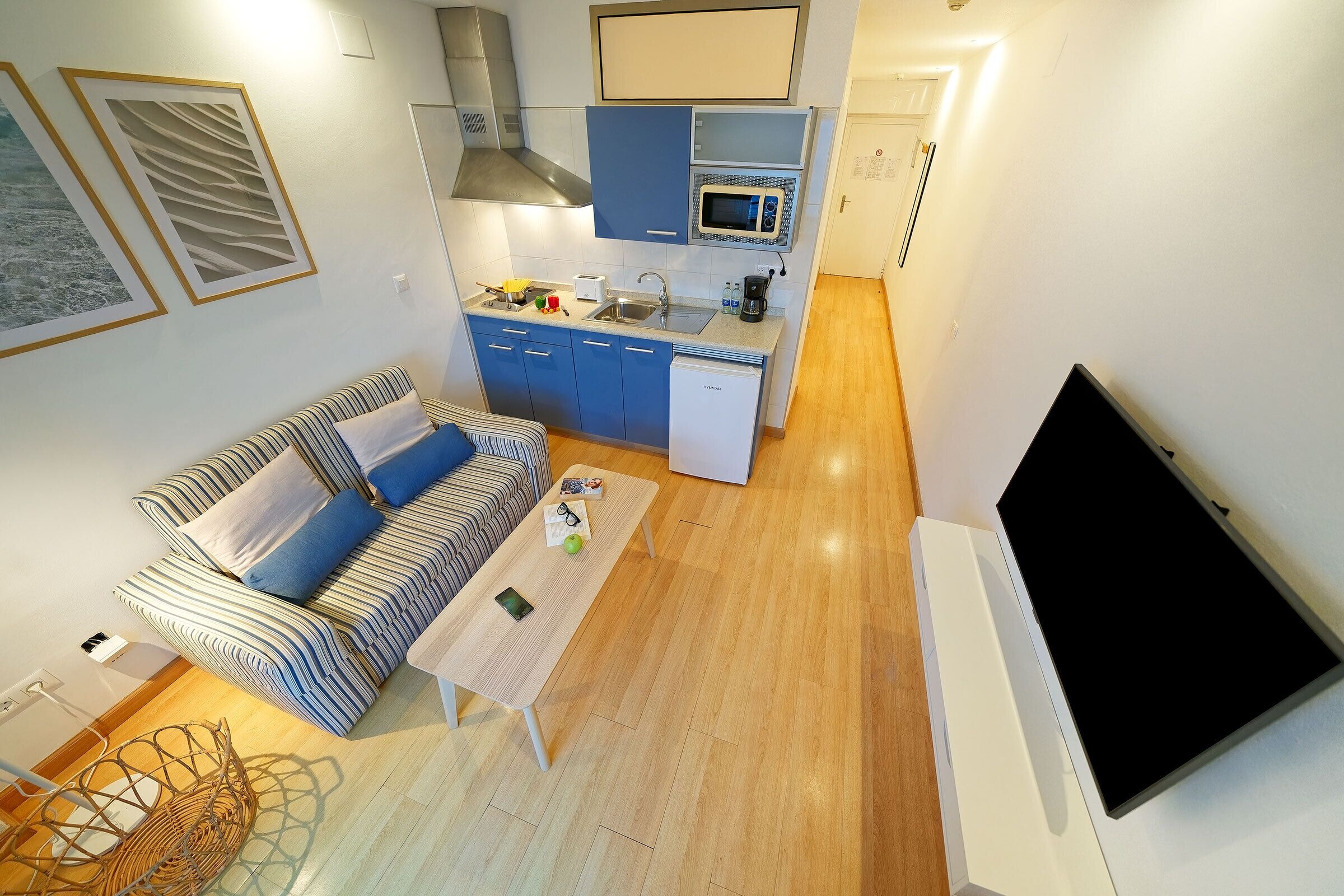 A compact living space with a kitchenette, a sofa, a coffee table, and a flat-screen TV.