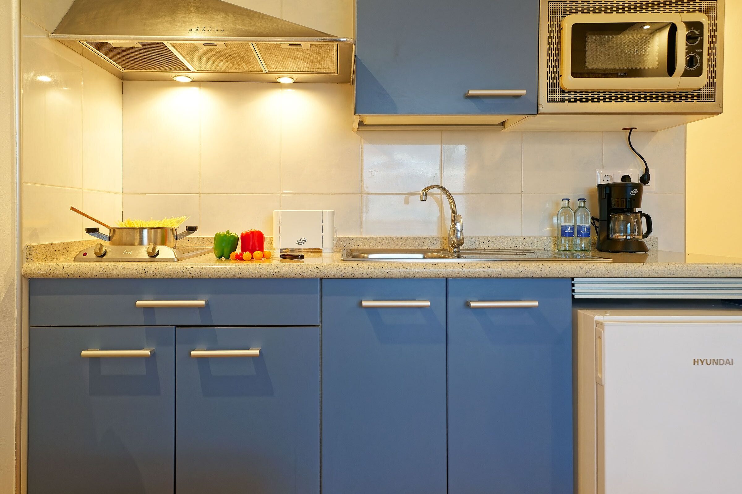 A kitchen with blue cabinets, a stainless steel range hood, a microwave, and a sink.