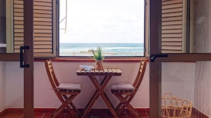 Un balcón con una mesa de madera y dos sillas, una planta en maceta y vista al mar.