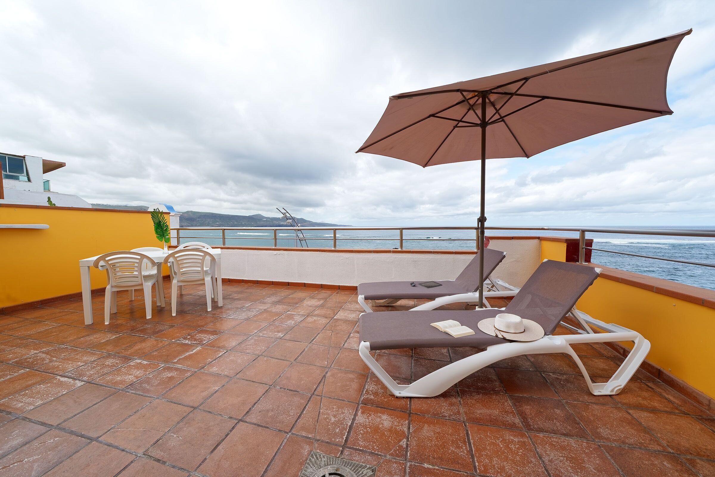 A terrace with a table and chairs, a sun umbrella, and a view of the sea.