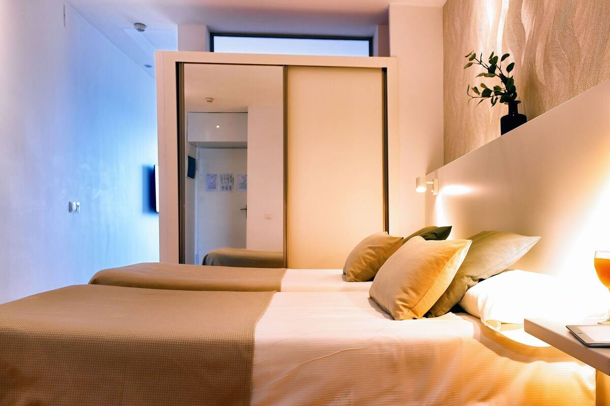 A modern hotel room with a large bed, a bedside table, and a view through an open door.