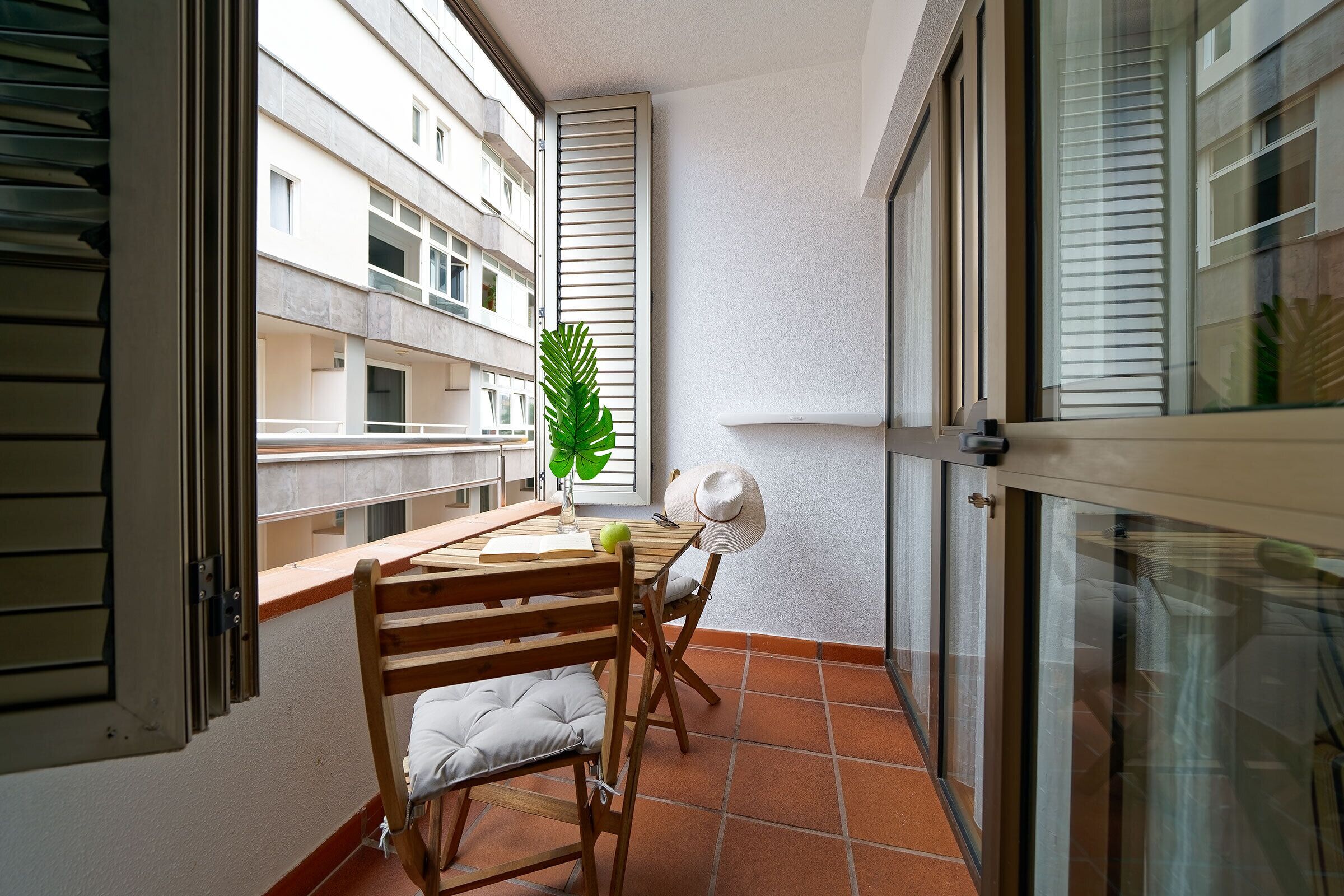 Un balcone con un tavolo di legno, due sedie, una pianta in vaso e un cappello sul tavolo.