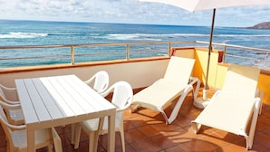 Una terraza con una mesa, sillas, un parasol y vistas al océano.