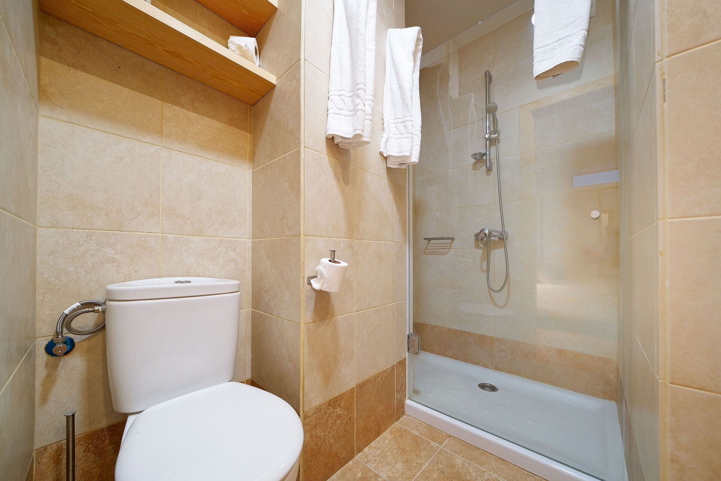 Un bagno con il water, una doccia con porta in vetro e un portascopevoli.