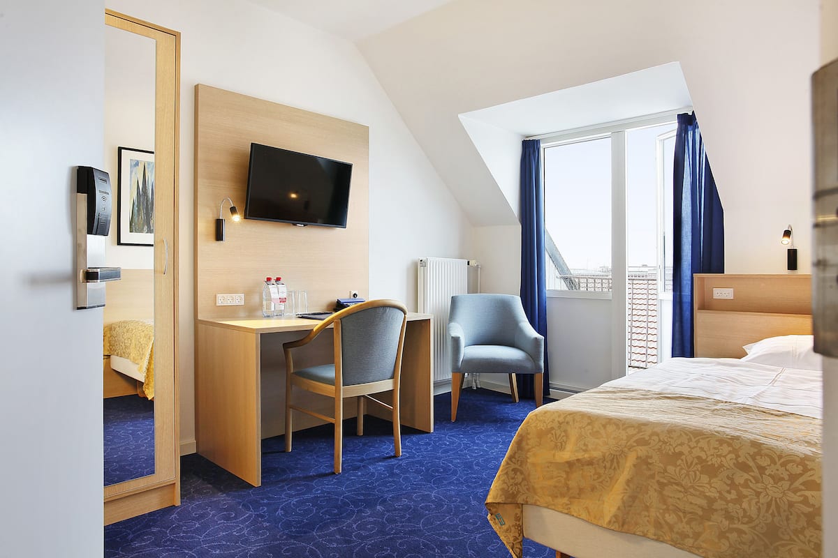 Hotellihuone, jossa on sänky, työpöytä tuolilla, televisio ja suuri ikkuna, jossa on verhot.