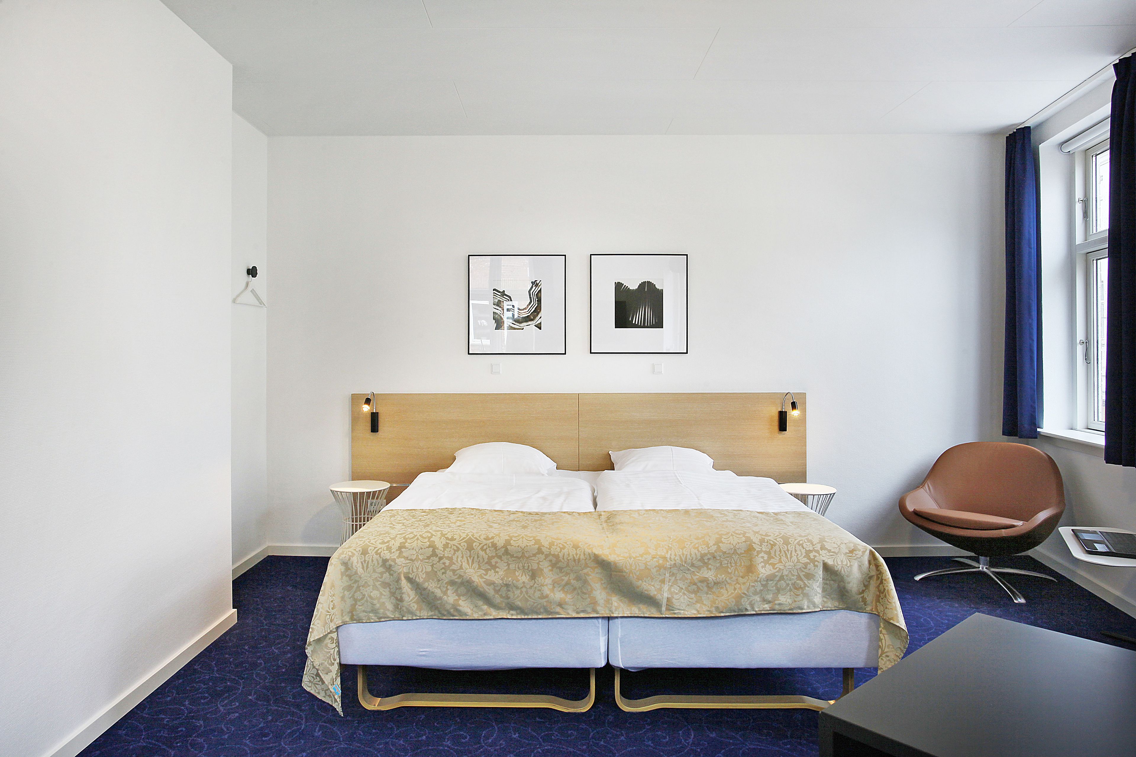 A hotel room with a double bed, a desk with a chair, two bedside tables, and two framed pictures on the wall.