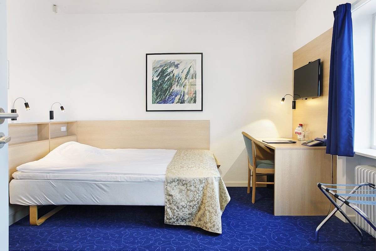 Hotellihuone, jossa on sänky, työpöytä, tuoli ja seinälle asennettu televisio.