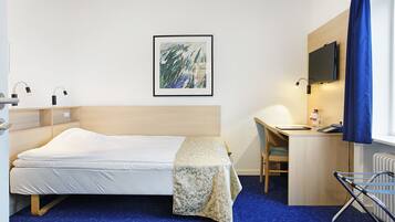 A hotel room with a bed, desk, chair, and a TV mounted on the wall.