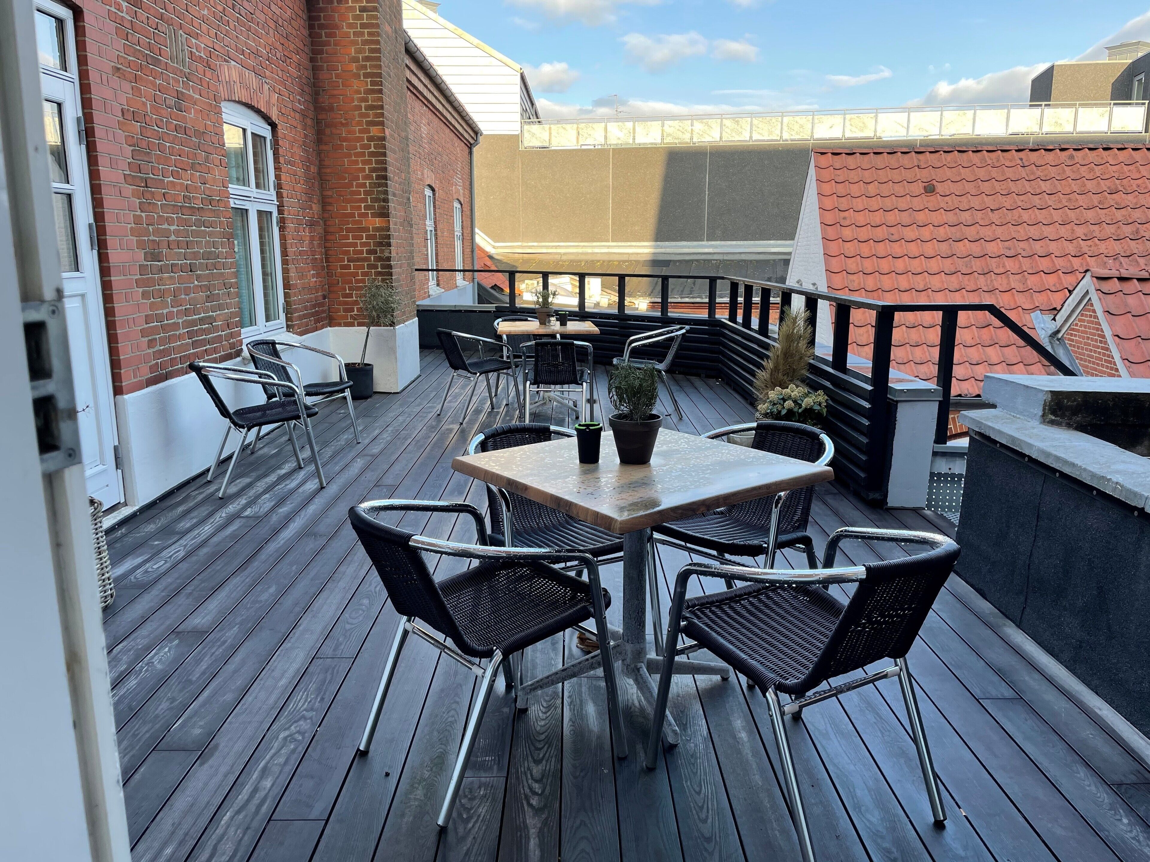 En træterrasse med et bord og stole, omgivet af murstensvægge og gelænder af metal.