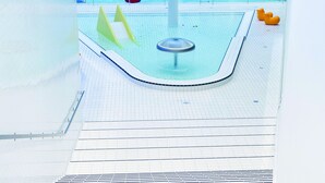 Ein großes Hallenbad mit mehreren Bahnen, einer zentralen Whirlwanne und bunten Schwimmspielzeugen.