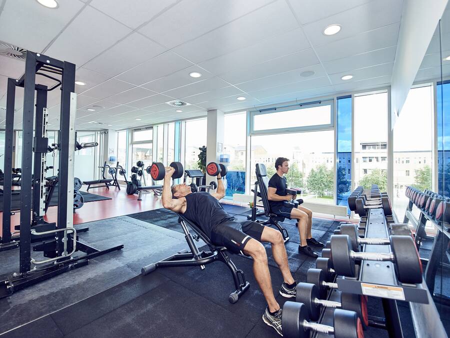 A gym with weightlifting equipment, large windows, and a view of buildings outside.