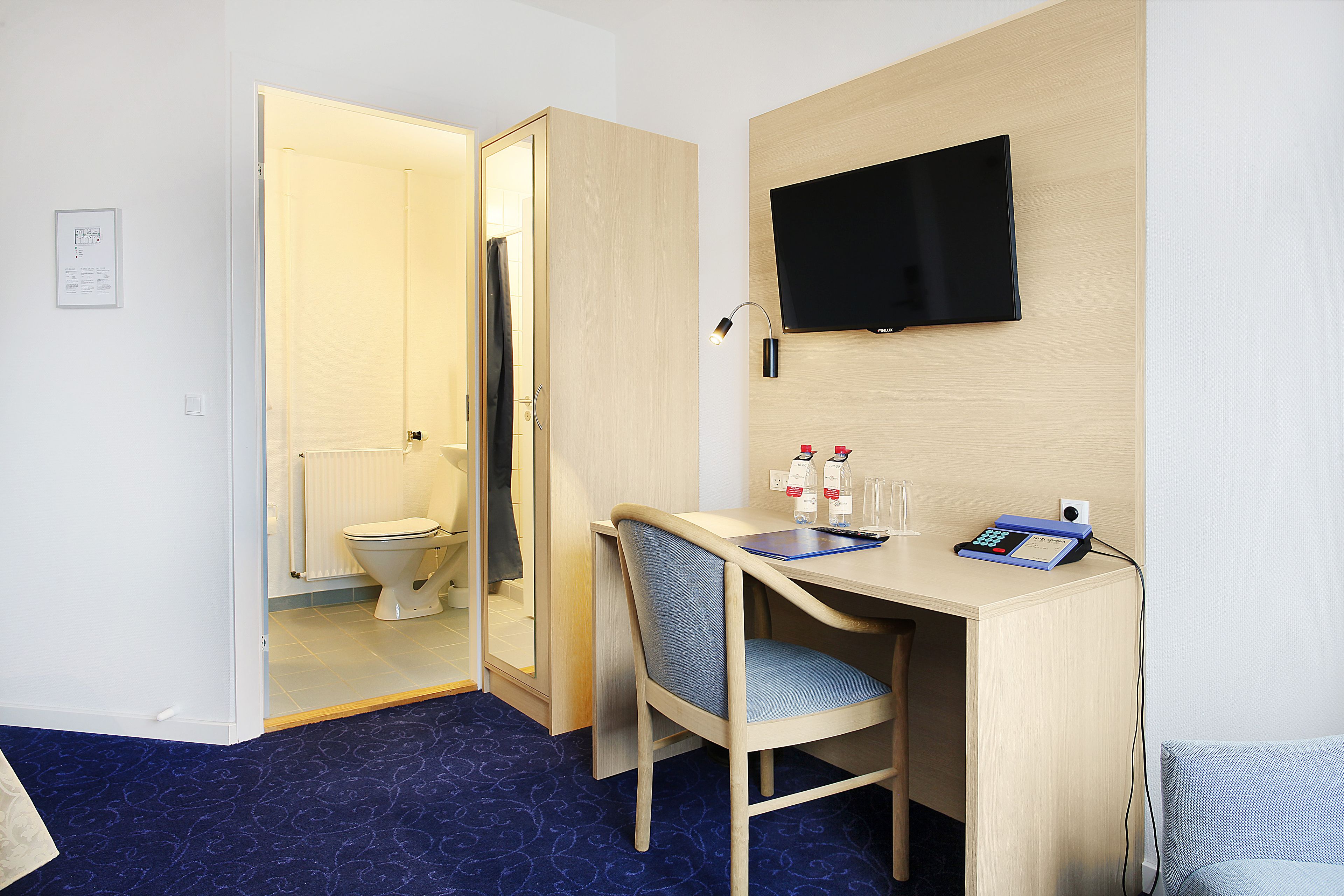 Een hotelkamer met een bureau, stoel, televisie en uitzicht op de badkamer.