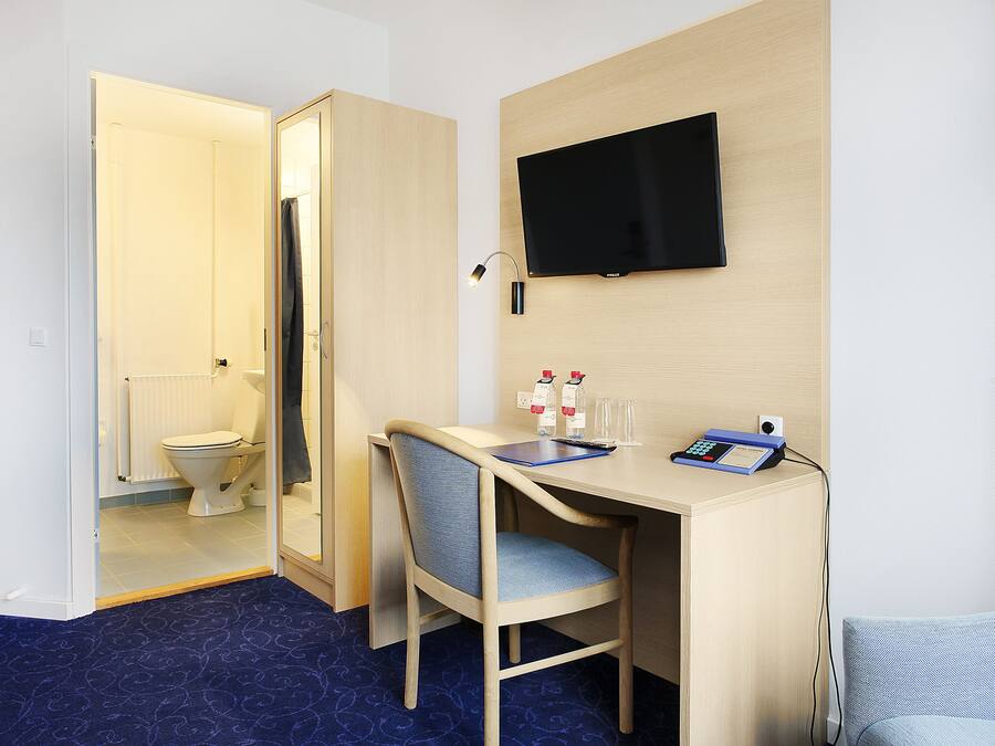 A hotel room with a desk, chair, television, and a view of the bathroom.