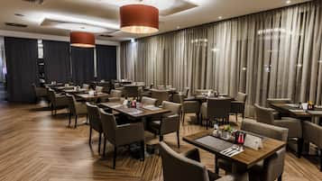 Ein stilvoller Hotel-Speiseraum mit mehreren Tischen und Stühlen, Holzböden und großen Fenstern mit Vorhängen.
