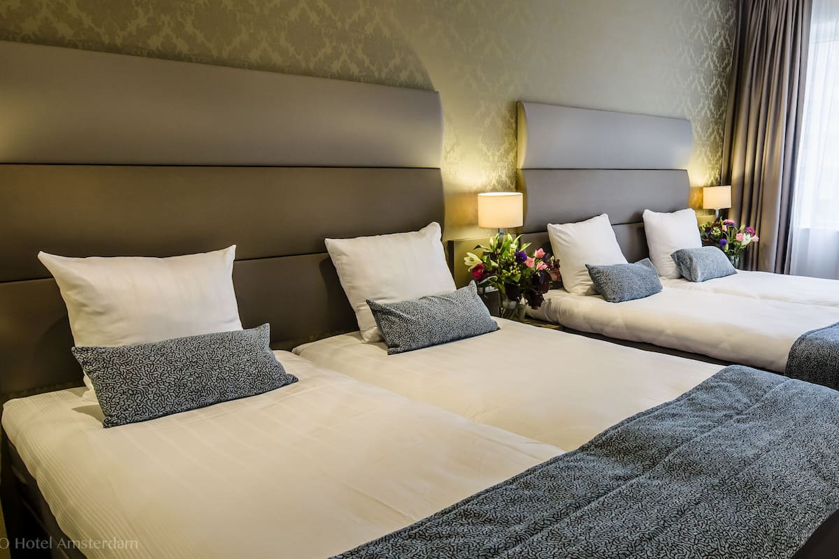 A hotel room with two beds, each with a headboard, bedside tables with lamps, and a vase with flowers.