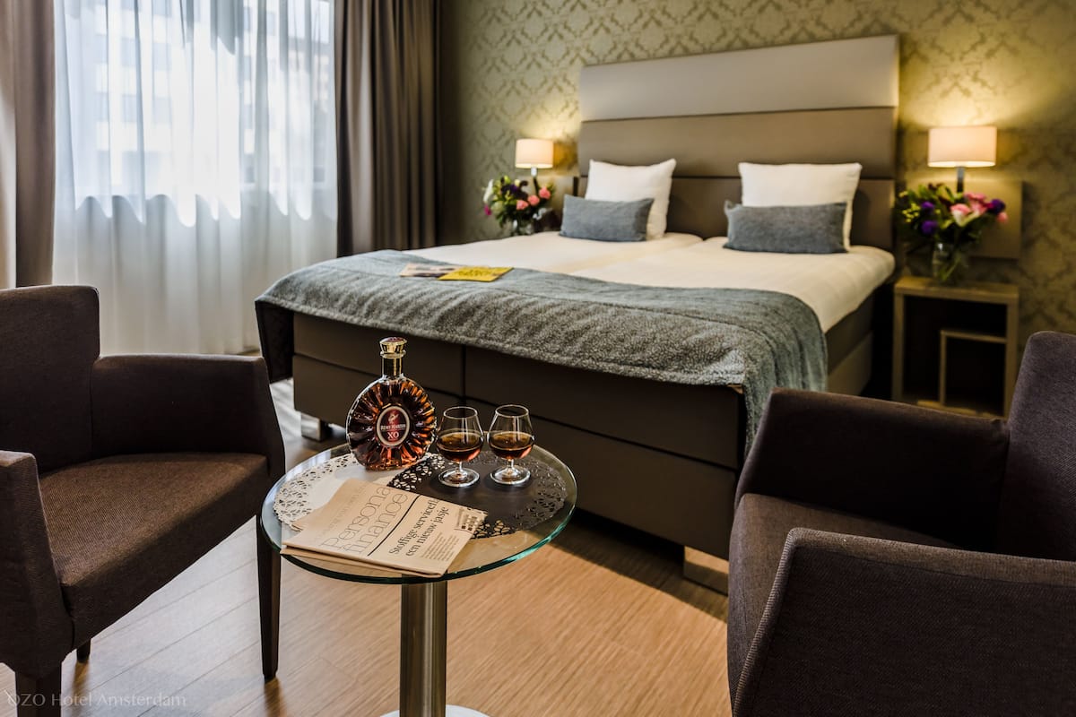 A hotel room with a bed, two bedside tables with lamps, a glass table with a menu, and two chairs.