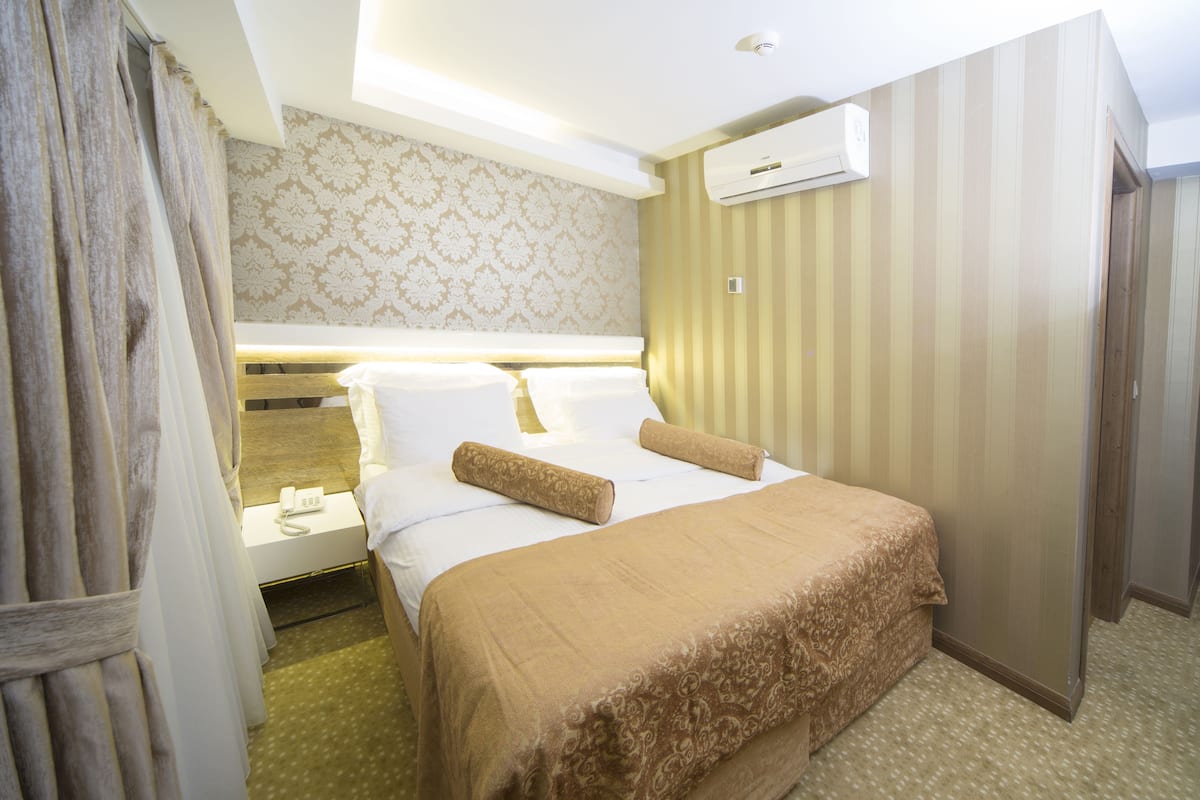 A hotel room with a bed, bedside table, and an air conditioning unit.