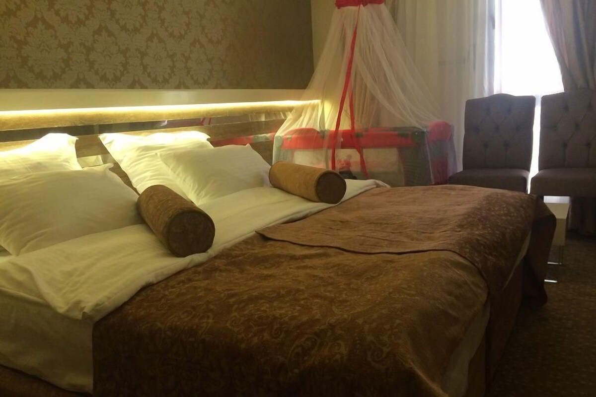 A hotel room with a bed, pillows, a canopy, and a chair.