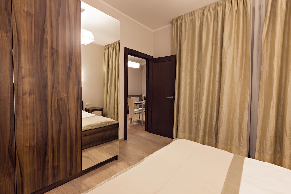 A hotel room with a wooden wardrobe, a bed, a desk, and a chair.