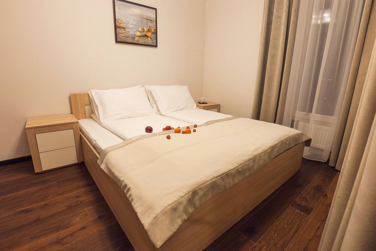A neatly made bed with white linens, a small bedside table with a lamp, and a painting on the wall.