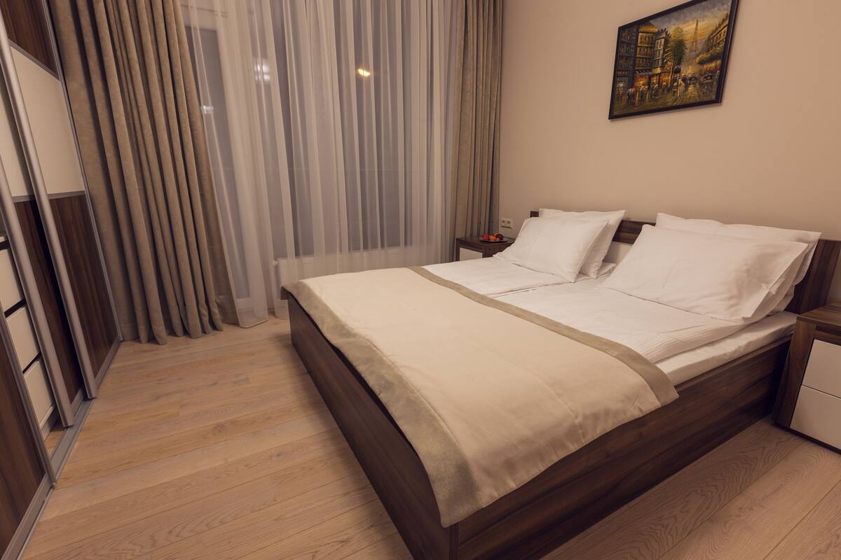 A neatly made bed with white linens, a wooden headboard, and a nightstand with a lamp.