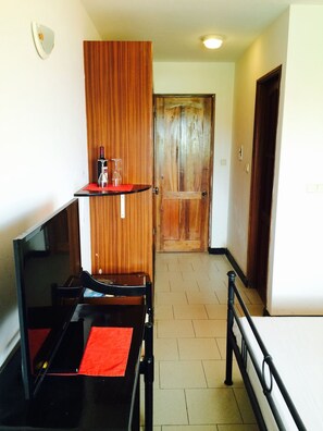 A hotel room with a wooden wardrobe, a small table with a red placemat, a chair, and a bed with a white mattress. - Blue Bell Hotel (Ribeira Grande)