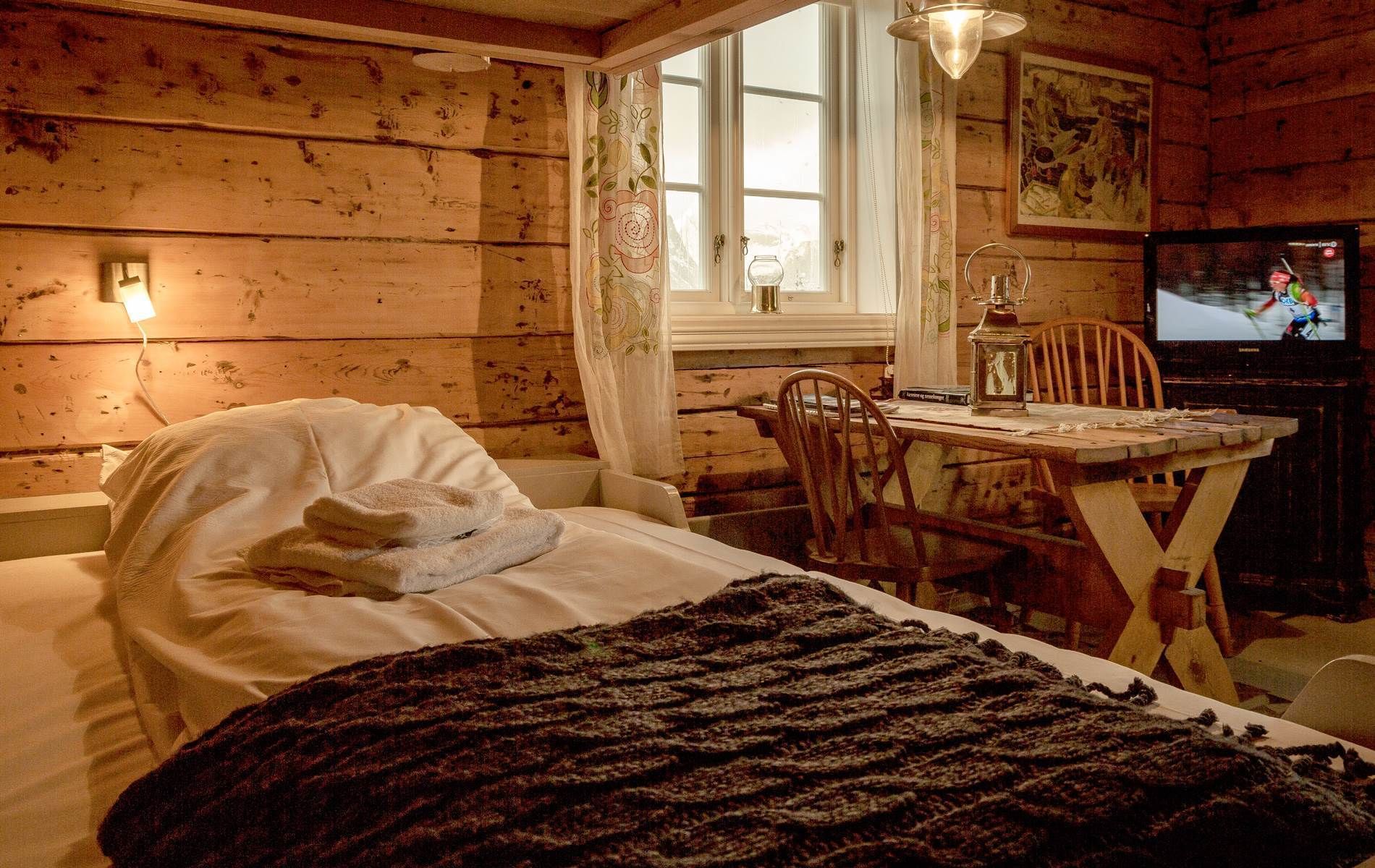 Una habitación acogedora con una cama, una mesa con una lámpara, una silla y un televisor.