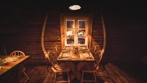 Een houten eettafel gedekt voor vier personen, met stoelen, een raam met uitzicht op een huis en een hanglamp.