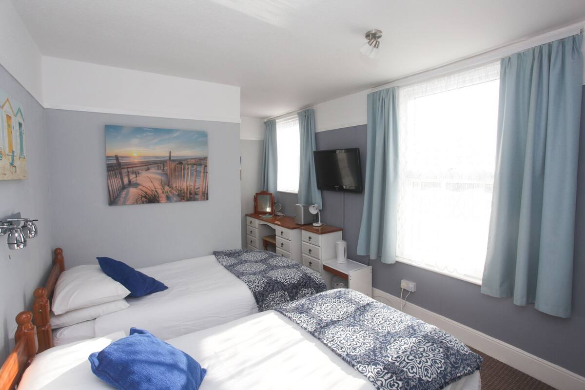 Habitación de hotel con dos camas, un escritorio, un televisor y un cuadro de una playa.