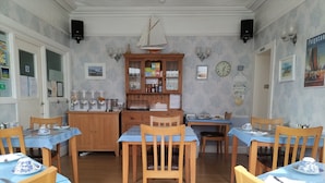A dining area with wooden tables and chairs, a wooden cabinet with glass doors, and wall-mounted light fixtures. - The Clydesdale (Paignton)