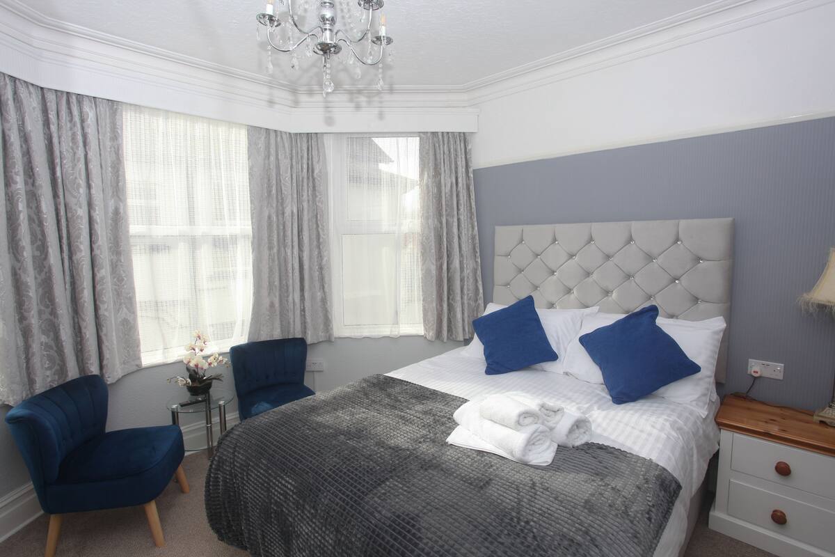 Una habitación de hotel con una cama grande, una silla, una mesita pequeña y una mesita de noche.