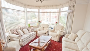 A living room with a red patterned carpet, white furniture, and large windows with blinds. - The Clydesdale (Paignton)