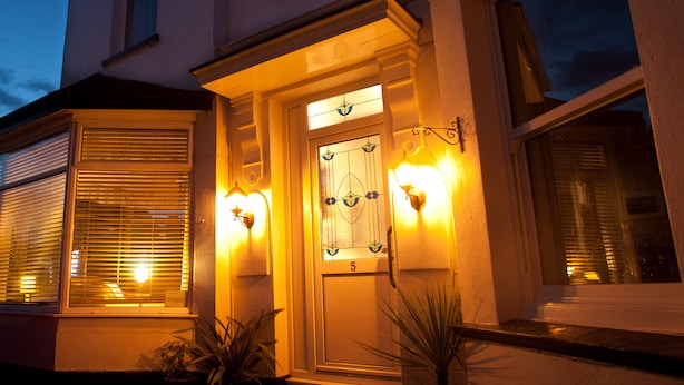 A building entrance with a door marked '5', two lit wall sconces, and potted plants. - The Clydesdale (Paignton)
