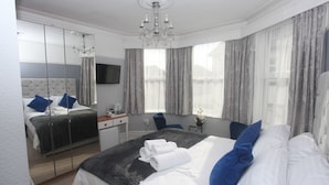 A hotel room with a large bed, a desk, a chair, a mirror, and a chandelier. - The Clydesdale (Paignton)
