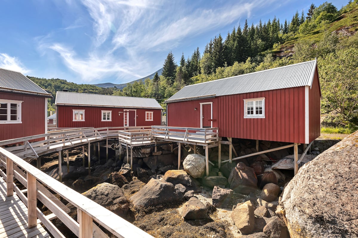 A red wooden building with a metal roof, a wooden deck, and a rocky foundation.