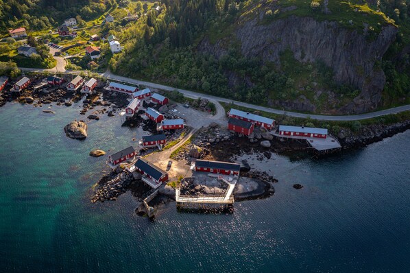 Vista aérea de un pueblo costero con edificios de techo rojo, un muelle y una carretera que lo atraviesa.