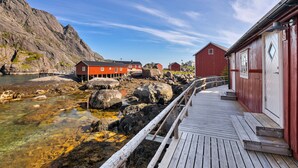 A wooden pier leading to a red building with a white door, set against a rocky coastline. - Lofoten Cottages (Flakstad)