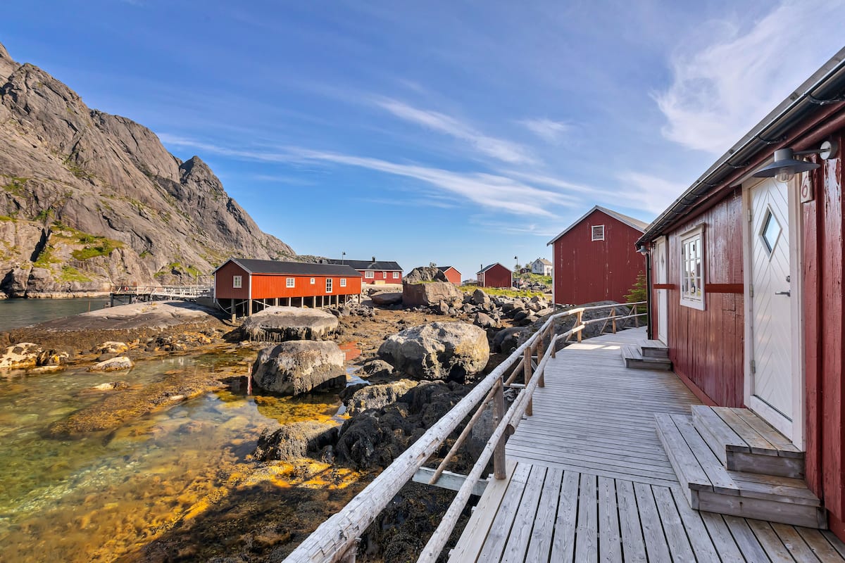 A wooden pier leading to a red building with a white door, set against a rocky coastline.