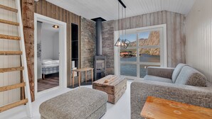 A cozy cabin interior with a wooden ladder, a sofa, a wooden chest, and a table. - Lofoten Cottages (Flakstad)