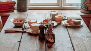 A wooden table with a meal set, a salt shaker, and a bottle, viewed through a window overlooking a body of water and hills. - Lofoten Cottages (Flakstad)