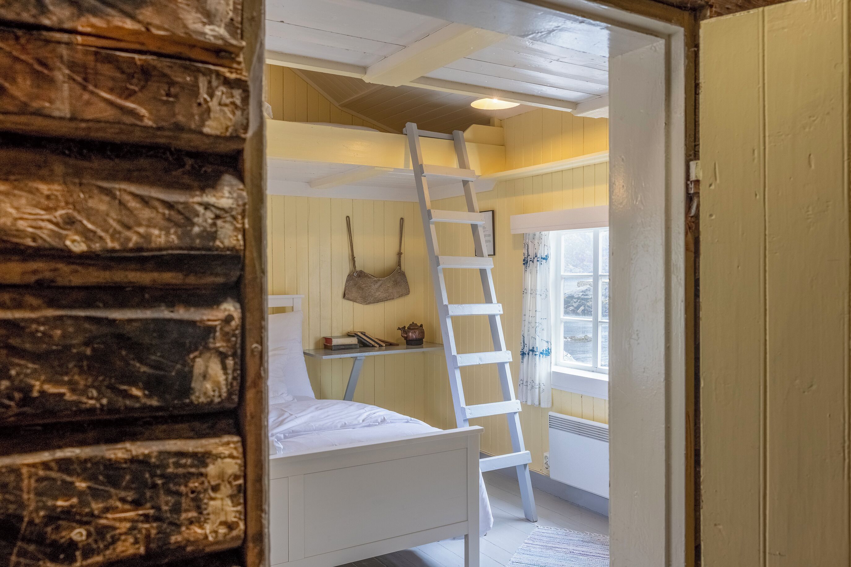 Une pièce avec un lit superposé, une échelle, une fenêtre avec des rideaux et un mur en bois rustique.