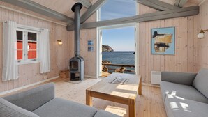 A cozy cabin with a wooden interior, a fireplace, and a view of the sea. - Lofoten Cottages (Flakstad)