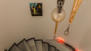 Un escalier en colimaçon, avec une bande lumineuse rouge le long de la rampe et un tableau accroché au mur.