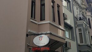 Un immeuble à plusieurs étages, sur lequel on peut lire l’inscription « The House of Tulpan », et un écran numérique affichant « 21.00.00 ».