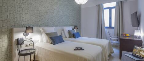 A hotel room with two beds, a desk with a laptop, a chair, a lamp, and a telephone.